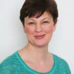 Frau mit kurzen braunen Haaren in grüner Bluse, lächelnd.