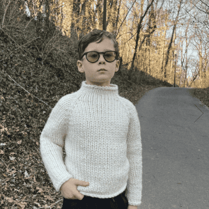 Junge mit Brille trägt weißen Pullover im Freien.