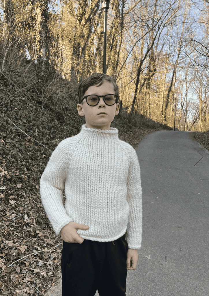 Junge mit Brille trägt weißen Pullover im Freien.