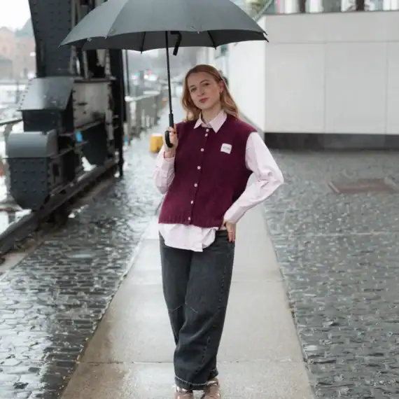 Frau mit Regenschirm auf nasser Straße, trägt lässigen Pullover und Jeans, bei regnerischem Wetter i.